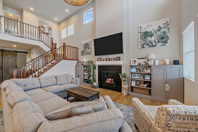 living area featuring wood finished floors, a barn door, a high ceiling, stairs, and a tile fireplace