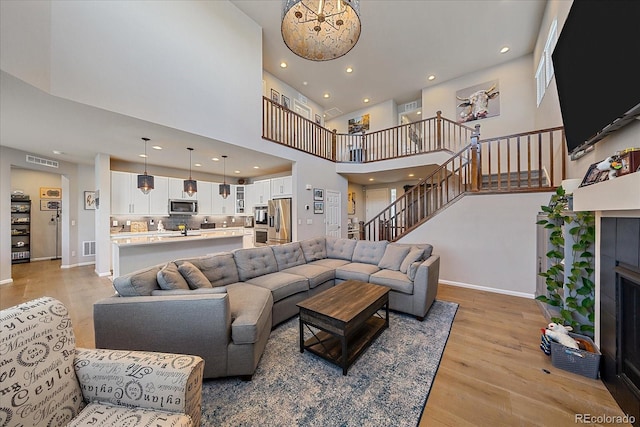 living room featuring baseboards, visible vents, a tile fireplace, stairs, and light wood-type flooring