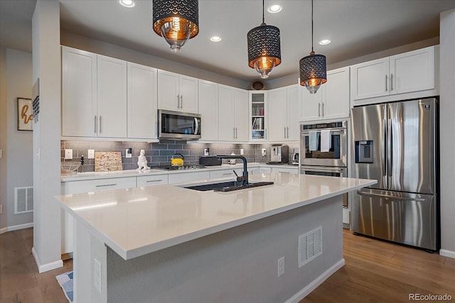 kitchen featuring tasteful backsplash, glass insert cabinets, wood finished floors, stainless steel appliances, and a sink