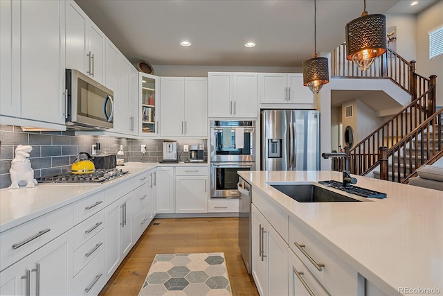 kitchen featuring a sink, light countertops, glass insert cabinets, appliances with stainless steel finishes, and backsplash