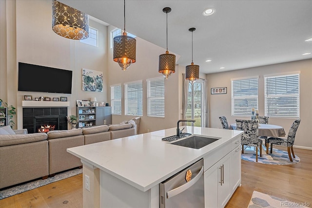 kitchen with a tiled fireplace, white cabinetry, light wood finished floors, a sink, and stainless steel dishwasher