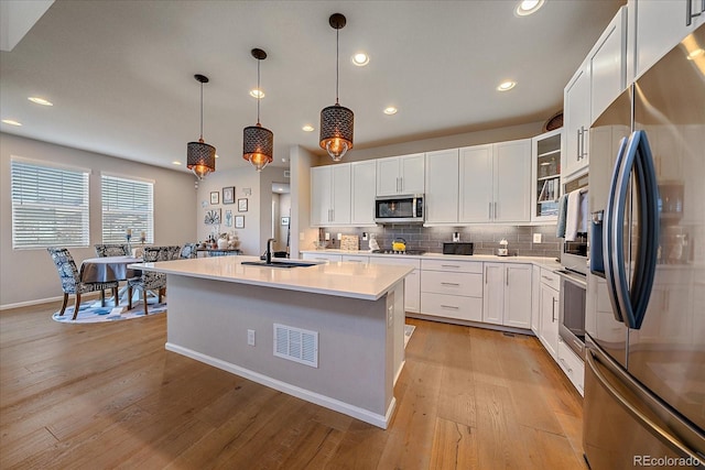 kitchen with light wood finished floors, a sink, decorative backsplash, light countertops, and appliances with stainless steel finishes