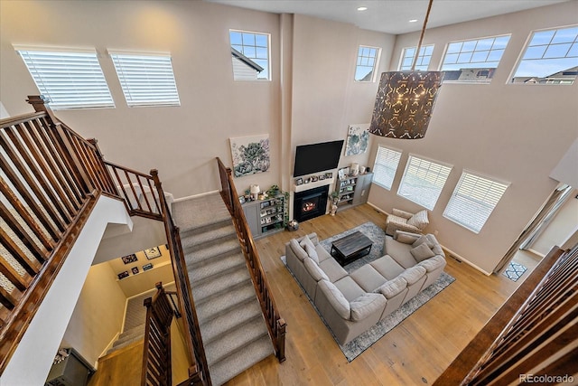 living area featuring a lit fireplace, a high ceiling, wood finished floors, and stairs