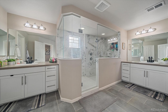 full bathroom with a marble finish shower, visible vents, and a sink