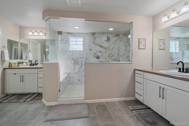 full bathroom featuring two vanities, visible vents, a tile shower, and a sink