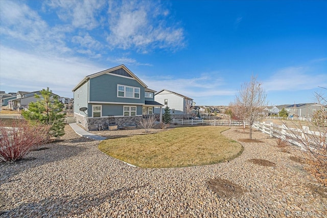 back of house featuring a yard, fence, stone siding, and a residential view