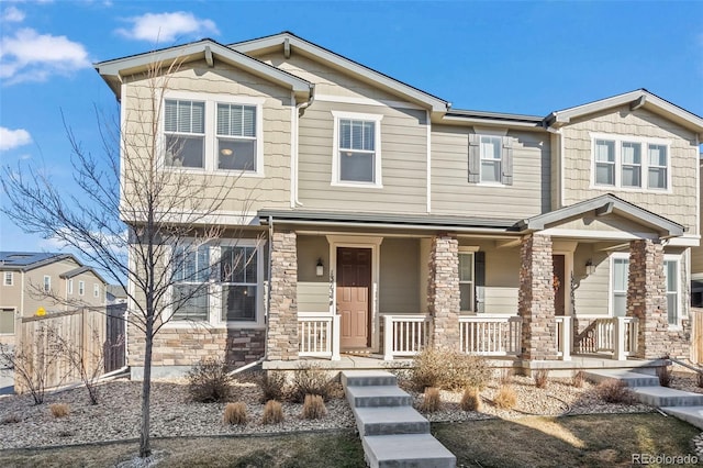 view of front of home featuring stone siding, a porch, and fence