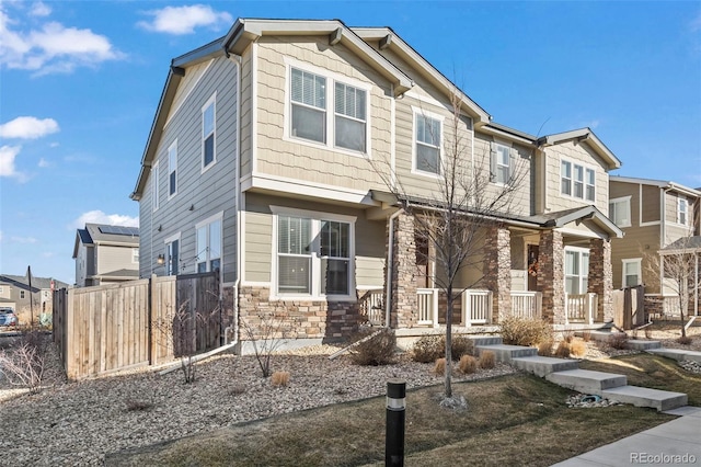 craftsman house with stone siding, a porch, and fence