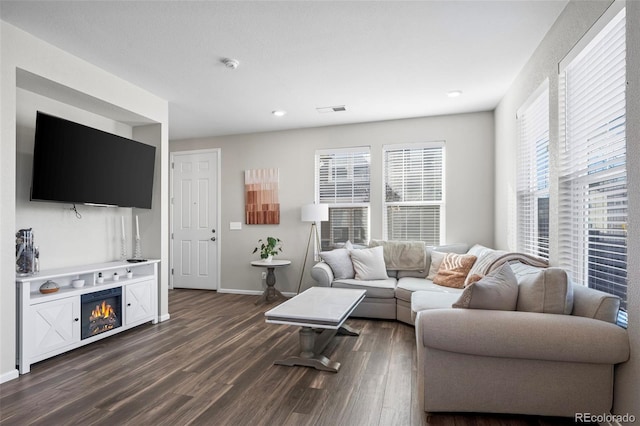 living room featuring a warm lit fireplace, dark wood-style flooring, visible vents, and baseboards