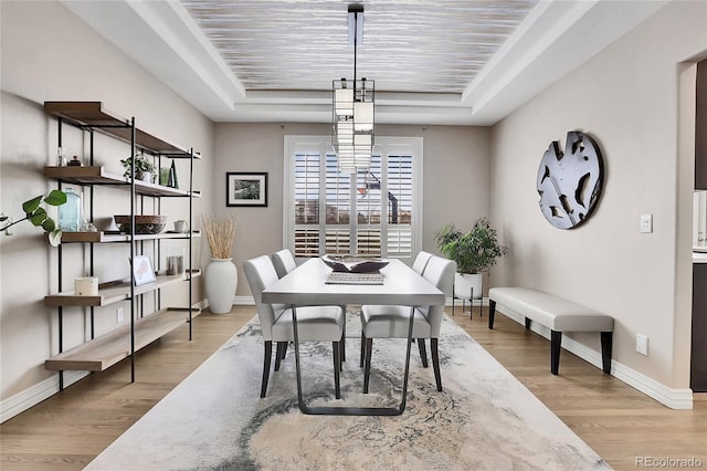 dining space featuring a raised ceiling and light wood-type flooring