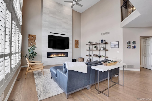 living room with a towering ceiling, light hardwood / wood-style floors, a large fireplace, and ceiling fan