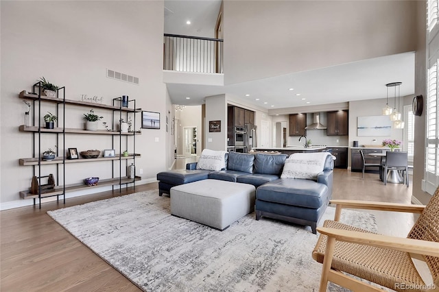 living room featuring sink, a towering ceiling, and light wood-type flooring