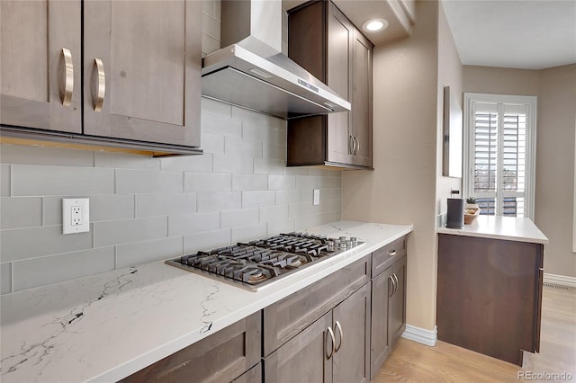 kitchen with light stone counters, wall chimney exhaust hood, stainless steel gas stovetop, and backsplash