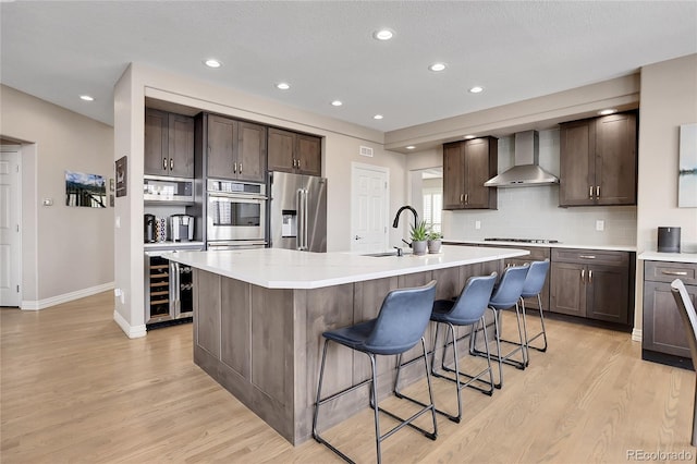 kitchen featuring appliances with stainless steel finishes, a breakfast bar area, wine cooler, a center island with sink, and wall chimney exhaust hood