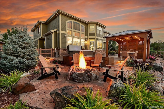 back house at dusk featuring a gazebo, a patio, and a fire pit