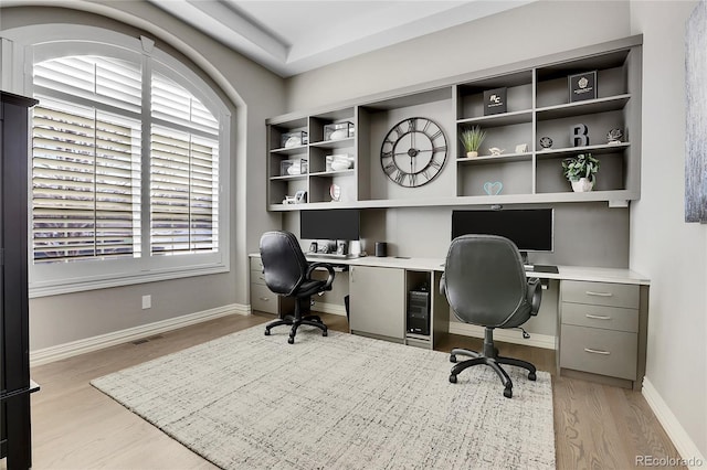 home office with built in desk and light hardwood / wood-style floors