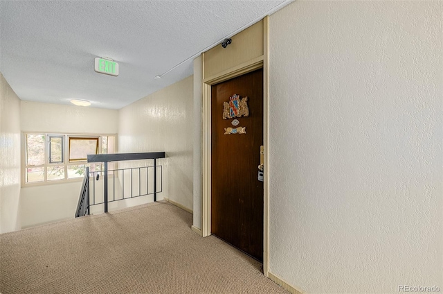 hall featuring light colored carpet and a textured ceiling