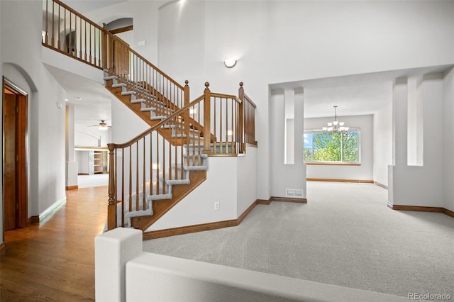 stairway featuring a high ceiling, baseboards, a chandelier, carpet floors, and ceiling fan