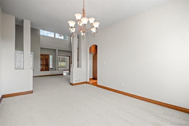 empty room featuring light colored carpet, arched walkways, baseboards, a chandelier, and a towering ceiling