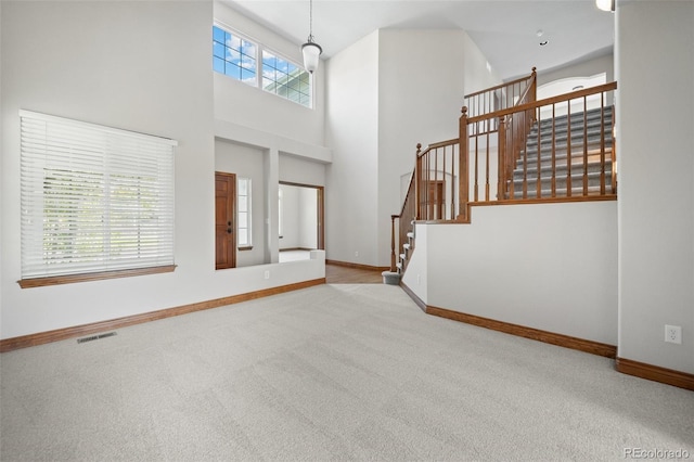 unfurnished living room featuring carpet flooring, baseboards, a towering ceiling, and stairs