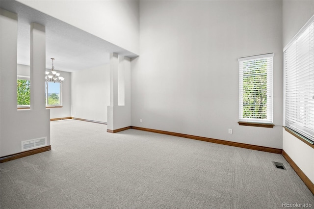 carpeted spare room featuring a chandelier, baseboards, and a high ceiling