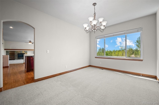 spare room with carpet, baseboards, a chandelier, arched walkways, and a fireplace