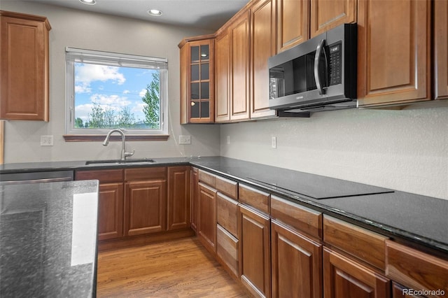 kitchen featuring stainless steel microwave, a sink, black electric cooktop, brown cabinetry, and light wood finished floors