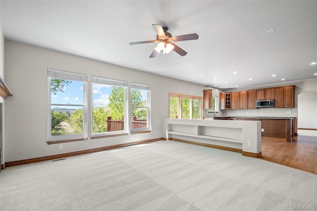 kitchen featuring stainless steel microwave, carpet flooring, ceiling fan, brown cabinets, and baseboards