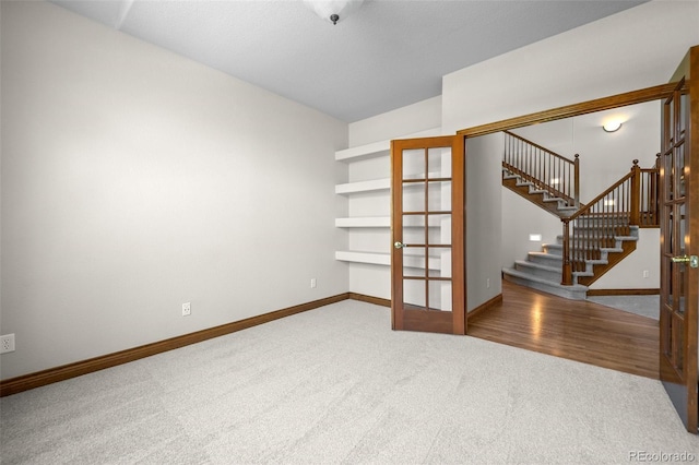 carpeted empty room with stairs, french doors, and baseboards