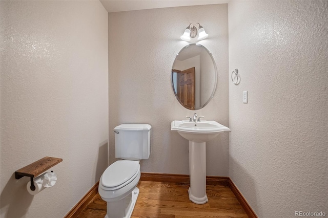 half bathroom featuring wood finished floors, toilet, and baseboards