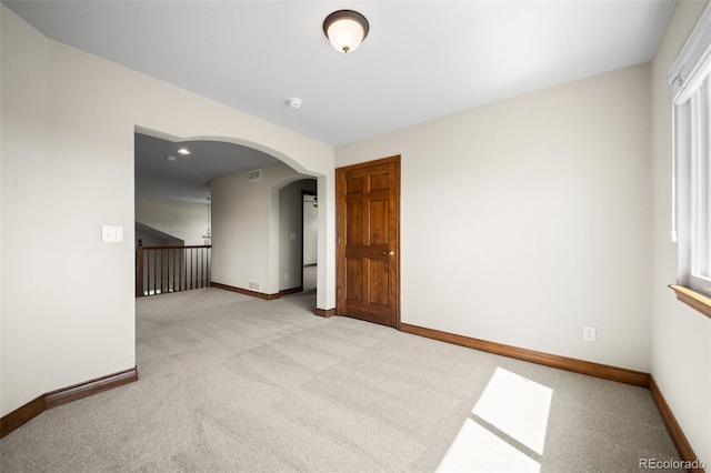 empty room featuring light carpet, arched walkways, and baseboards
