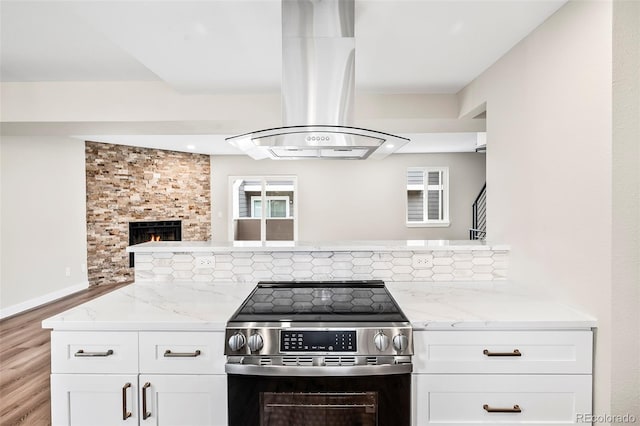 kitchen featuring electric range, island range hood, light stone countertops, white cabinets, and kitchen peninsula