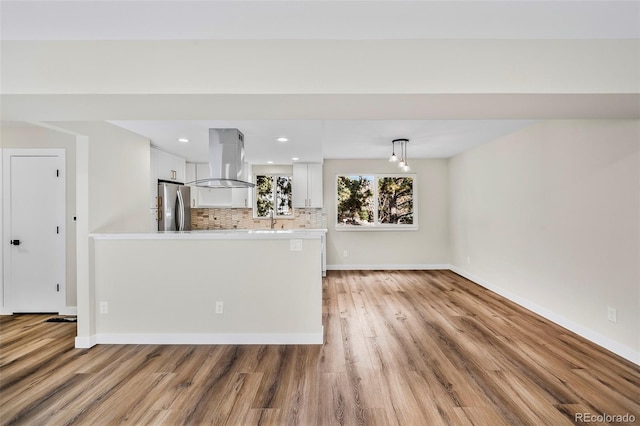 kitchen with white cabinetry, island range hood, stainless steel refrigerator, pendant lighting, and decorative backsplash