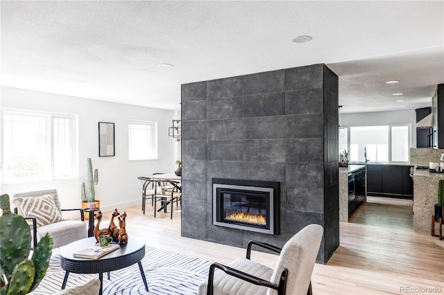 living room with a tile fireplace, a textured ceiling, and light wood-type flooring