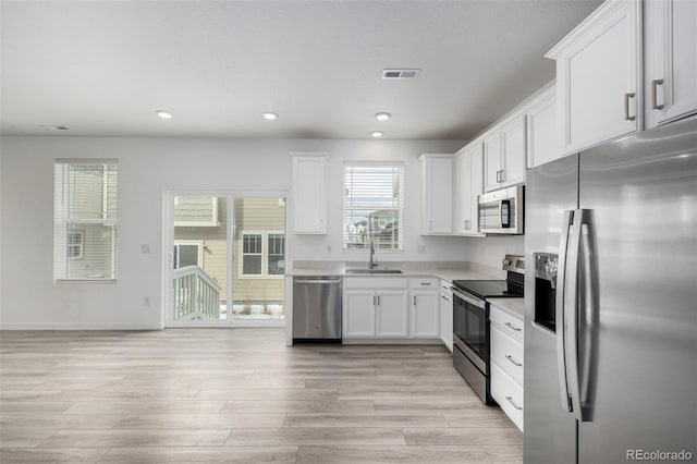 kitchen with light wood-type flooring, appliances with stainless steel finishes, sink, and white cabinets