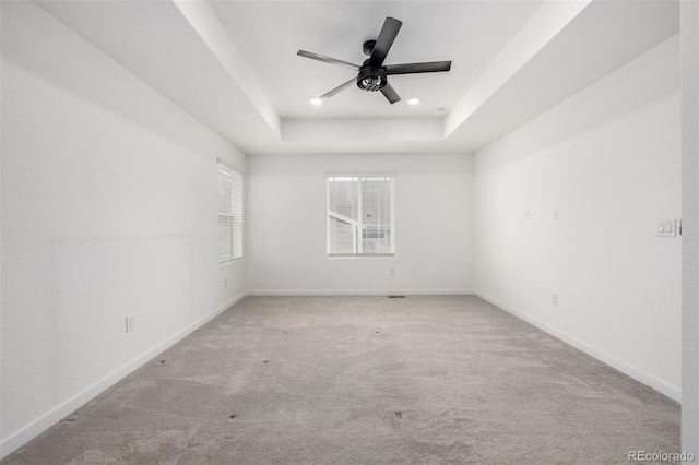 carpeted spare room with a raised ceiling and ceiling fan