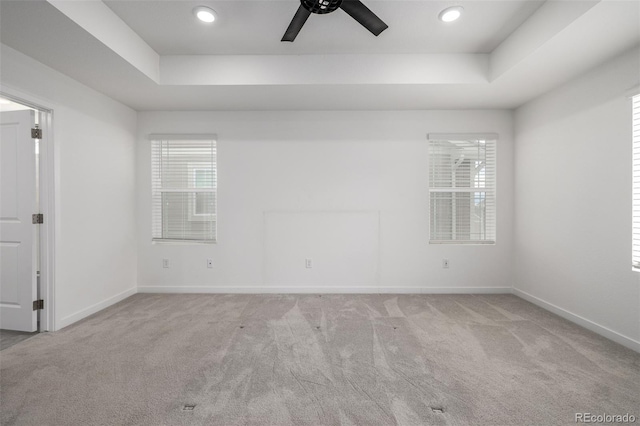 empty room featuring a raised ceiling, light colored carpet, and ceiling fan