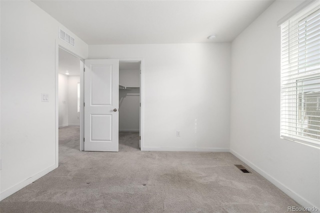 unfurnished bedroom featuring multiple windows, a walk in closet, and light colored carpet