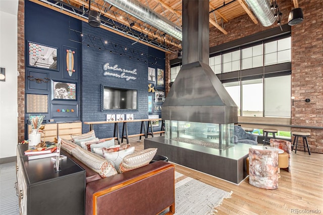 living room featuring hardwood / wood-style flooring, beam ceiling, a towering ceiling, brick wall, and a wood stove