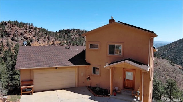 exterior space with a mountain view, a garage, stucco siding, a chimney, and driveway