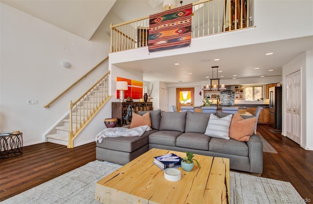 living room with stairs, dark wood-style flooring, baseboards, and a towering ceiling