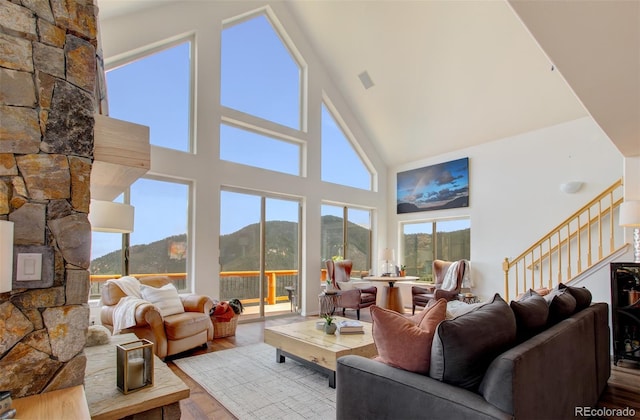 living room with a mountain view, stairs, high vaulted ceiling, wood finished floors, and a fireplace