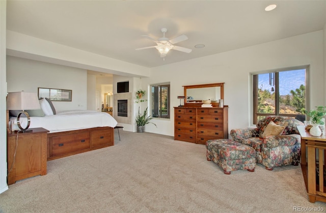 bedroom featuring light carpet, a ceiling fan, and a glass covered fireplace