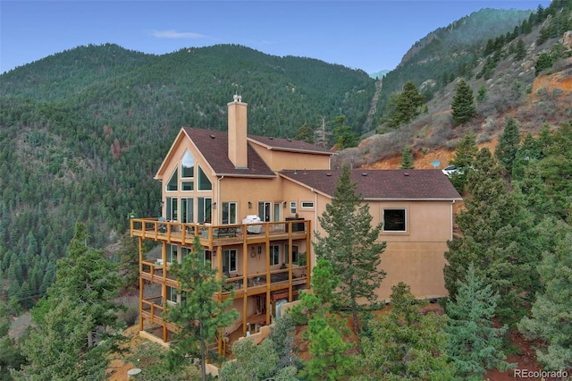 exterior space featuring a chimney, a deck with mountain view, stucco siding, and a wooded view