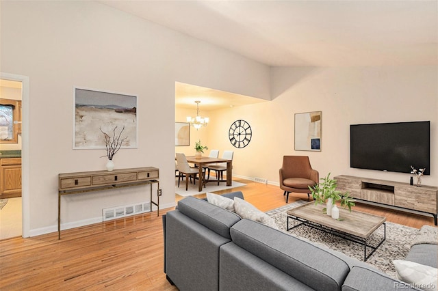 living area featuring a chandelier, light wood-type flooring, lofted ceiling, and baseboards