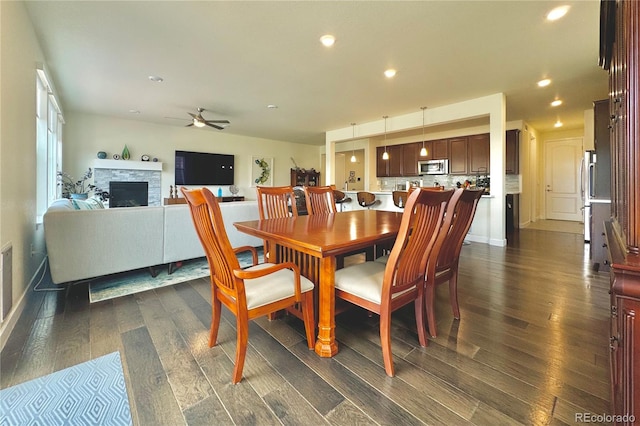 dining area with ceiling fan, dark hardwood / wood-style floors, and a stone fireplace