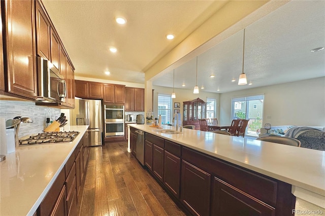 kitchen featuring appliances with stainless steel finishes, dark hardwood / wood-style floors, tasteful backsplash, sink, and pendant lighting