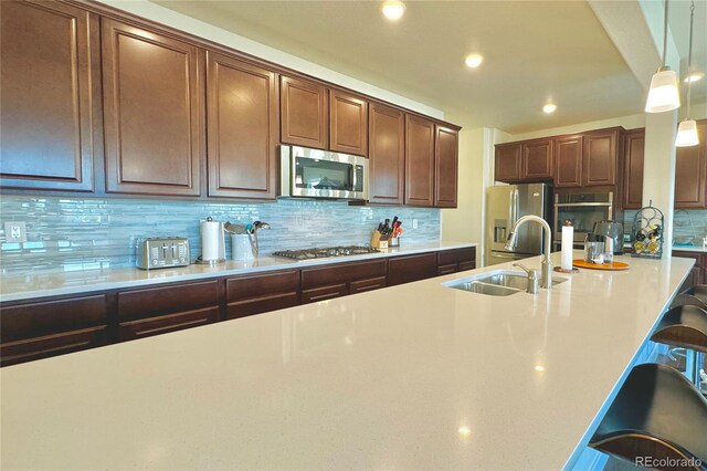 kitchen with a kitchen breakfast bar, backsplash, pendant lighting, sink, and stainless steel appliances