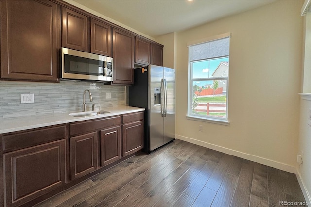 kitchen featuring appliances with stainless steel finishes, decorative backsplash, dark brown cabinetry, sink, and dark wood-type flooring