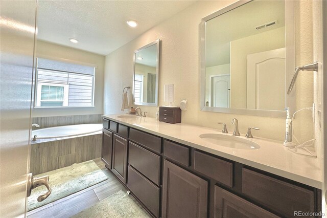 bathroom with tile patterned floors, double vanity, a textured ceiling, and a relaxing tiled tub